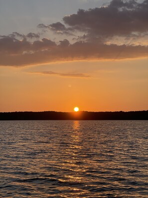 A sunset over a calm body of water with a silhouette of a distant landmass. - 2BR 2Bath Condo Tree top view located at Lake Ouachita.. (Mount Ida)