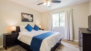 A bedroom with a bed, nightstands, a ceiling fan, a window with curtains, and a dresser.