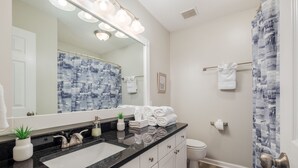 A modern bathroom with a black countertop sink, white cabinets, a large mirror, and a shower curtain with a blue pattern.