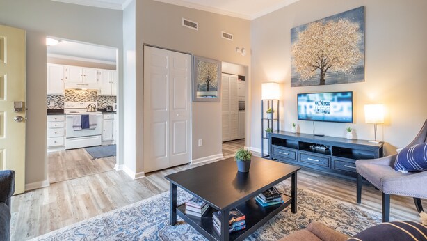 A modern living room with a flat-screen TV, a coffee table with books, a sofa, and a painting of a tree.