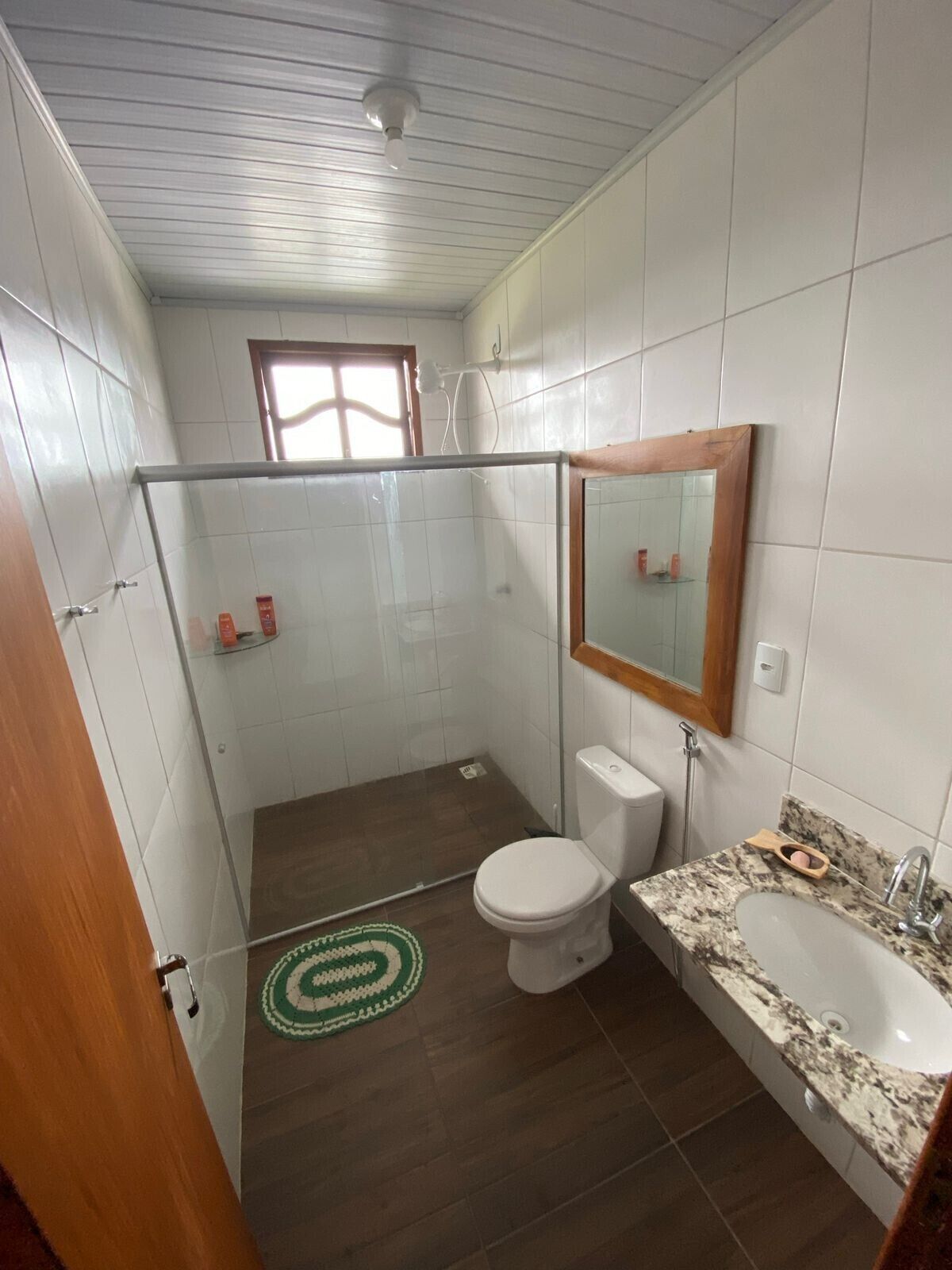 Een badkamer met een douchecabine van glas, een toilet, een wastafel met een marmeren blad en een spiegel met houten lijst.