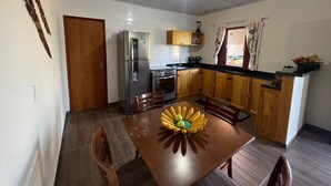 Una cocina compacta con armarios de madera, un refrigerador de acero inoxidable, un horno integrado y una mesa de comedor con un centro de mesa decorado con frutas.