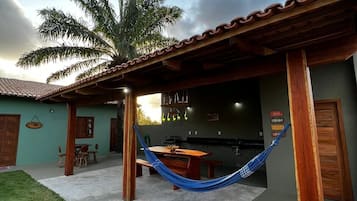 A patio area with a hammock, a dining table, and a kitchen visible through an open door.