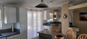 Una cocina con armarios blancos, una mesa de comedor con sillas, un dispensador de agua y un reloj en la pared.