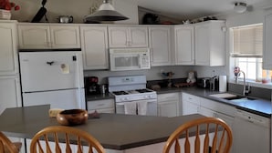 Una cocina con armarios blancos, microondas, estufa y pileta.