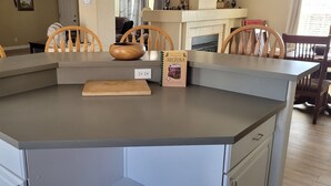 Una isla de cocina con encimera gris, sillas de madera, tabla de cortar y un libro de cocina titulado 'Best of the Best ARIZONA COOKBOOK'.