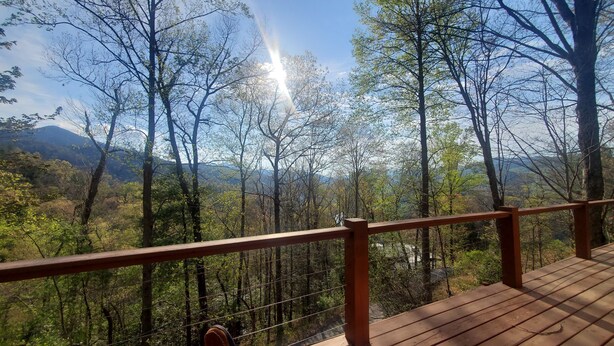 A wooden deck with a railing overlooking a forested landscape with mountains in the distance.