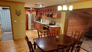 A modern kitchen with wooden cabinets, stainless steel appliances, and a dining area with a wooden table and chairs.