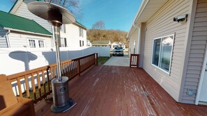Une terrasse en bois avec un radiateur métallique, des maisons au revêtement blanc et un ciel dégagé.
