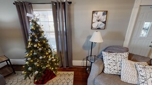 Een woonkamer met een kerstboom, een lamp en een deur met een bordje.
