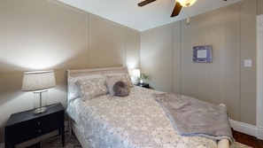 Ein Schlafzimmer mit Bett, Nachttisch, Lampe, Deckenventilator und einem gerahmten Bild an der Wand.