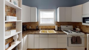 A kitchen with white cabinets, a double sink, a stove, and a window with blinds.
