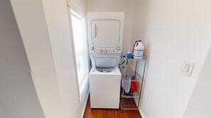 A compact laundry room with a front-loading washing machine and a metal shelf holding cleaning supplies.