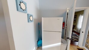 Eine kleine Küche mit einem weißen Kühlschrank, einem Besen und zwei Wanddekorationen.