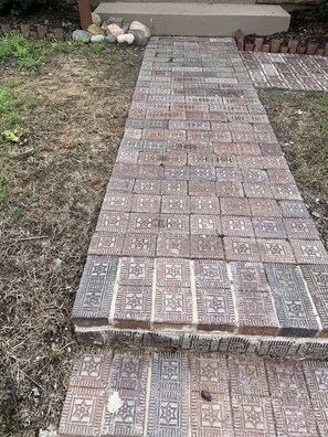A paved pathway with intricate tile patterns leading to a concrete structure.