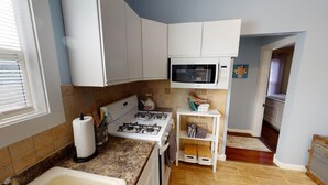 Une cuisine compacte avec des meubles blancs, une cuisinière à gaz, un four à micro-ondes et un petit plan de travail.