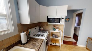Une cuisine compacte avec des meubles blancs, une cuisinière à gaz, un four à micro-ondes et un petit plan de travail.