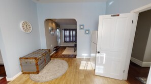 Een kamer met een houten vloer, een witte deur, een klok aan de muur en een koffer.