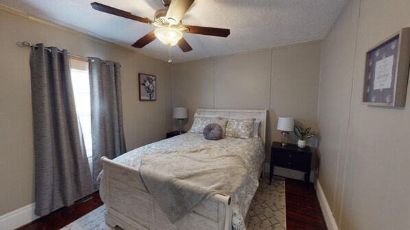 A bedroom with a bed, a ceiling fan, a nightstand, a lamp, and a framed picture on the wall.