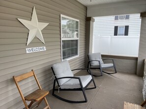 A covered porch with two rocking chairs and a wooden bench. A large star decoration and a 'WELCOME' sign are mounted on the wall.
