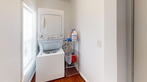 Une buanderie équipée d’un lave-linge, d’un étendoir et d’étagères contenant des produits de nettoyage.