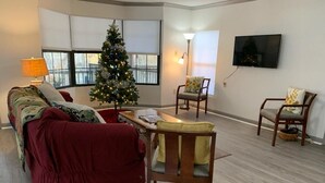 Ein Wohnzimmer mit Weihnachtsbaum, einer Couch, zwei Sesseln, einem Couchtisch und einem an der Wand befestigten Fernseher.