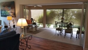 Una habitación amplia con una mesa y sillas de vidrio, una lámpara y vistas al verdor exterior.