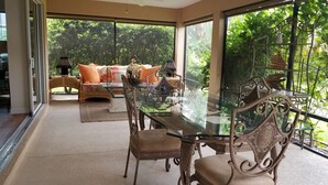 Una habitación amplia con una mesa de vidrio para comer, sillas de mimbre y un sofá con cojines estampados.