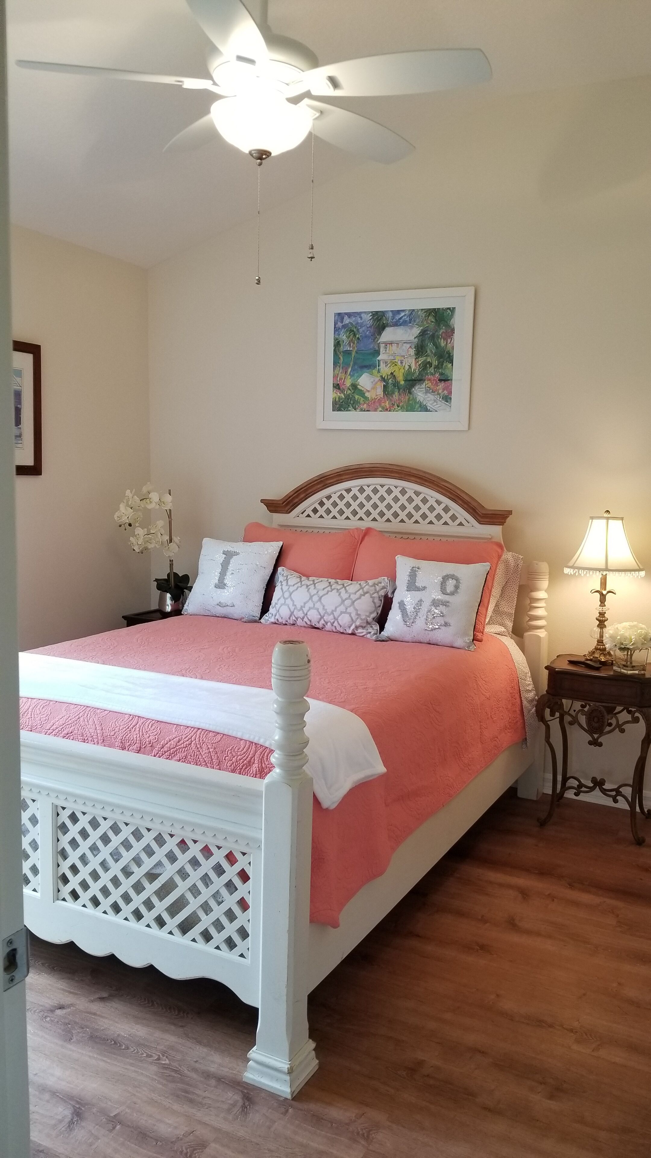 Une chambre à coucher avec un lit, un ventilateur de plafond, une table de chevet avec une lampe et un tableau au mur.