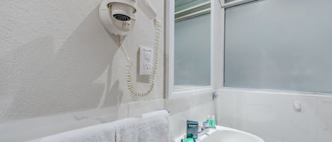A bathroom with a white sink, a towel, a security camera, and a window with frosted glass.