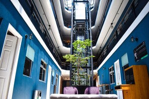 Interior moderno de un hotel con un hueco central para el ascensor, un árbol en maceta y una mesa de recepción.