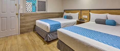Habitación de hotel con dos camas, suelo de madera, ventana con celosía decorativa y una puerta.