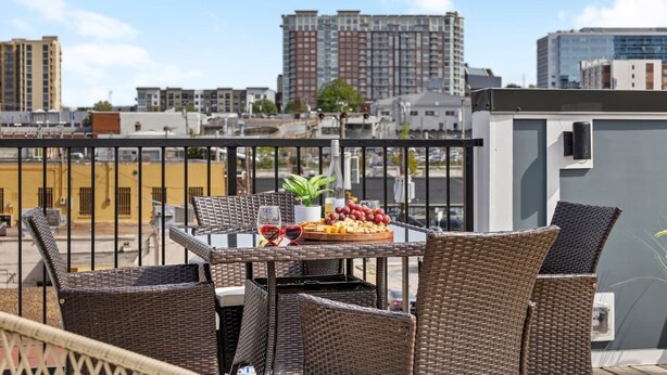 Ein Balkon mit Korbmöbeln, einem Tisch mit Obstplatte und Blick auf die Stadt.
