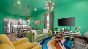 Ein modernes Wohnzimmer mit grüner Wand, einem Flachbildfernseher, einer Couch und einem Couchtisch.