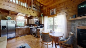 Cozy cabin-style kitchen with a stone fireplace, stainless steel appliances, and a dining table for two.