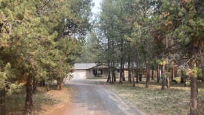 A gravel driveway leading to a single-story building with a garage, surrounded by pine trees. - Wooded river retreat near Mt. Bachelor and Bend (Bend)