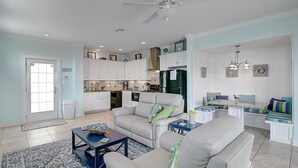 A spacious living room with a large sofa, a coffee table, and a dining area with a bench. - Sea the View Casita-ADA access + heated community pool.hot tub,beach boardwalk (Port Aransas)