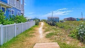 A pathway leading to a building with a balcony, surrounded by greenery and a clear sky. - Sea the View Casita-ADA access + heated community pool.hot tub,beach boardwalk (Port Aransas)