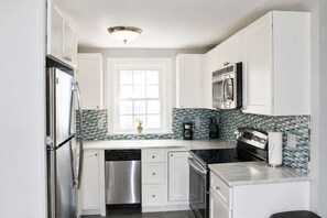 A modern kitchen with white cabinets, stainless steel appliances, a window, and a backsplash with blue tiles.