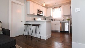 A compact kitchen with white cabinets, a microwave, and a dishwasher. There are two stools near the kitchen counter.