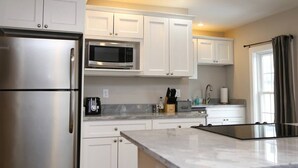 A modern kitchen with white cabinets, stainless steel appliances, and a marble countertop. - Beautiful Lake Winnipesaukee Getaway in Wolfeboro (Wolfeboro)