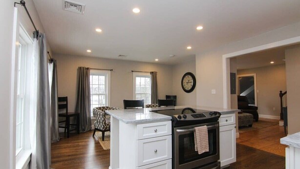 A modern kitchen with white cabinetry, a built-in oven, and a dining area with a table and chairs. - Beautiful Lake Winnipesaukee Getaway in Wolfeboro (Wolfeboro)