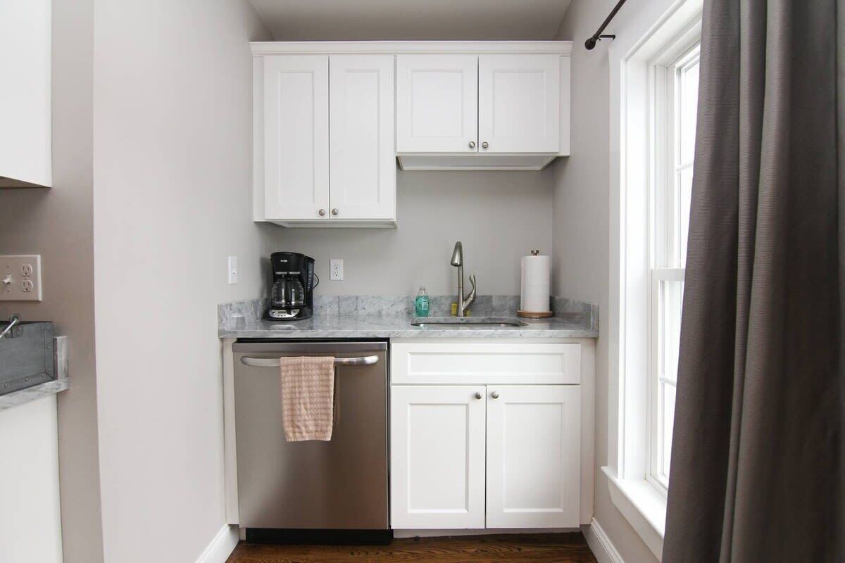 A compact kitchen with white cabinets, a dishwasher, a coffee maker, and a sink.