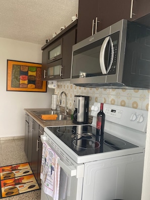 A kitchen with a microwave, stove, and coffee maker. There is a sink and a tiled backsplash.
