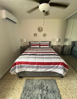 A bedroom with a bed, two bedside tables, a mirror, and a ceiling fan.