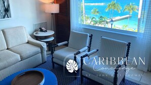 Habitación de hotel con vista al océano, un sofá, dos sillones, una mesita y una lámpara.