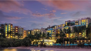 Un hotel con varias edificaciones, playa y palmeras.