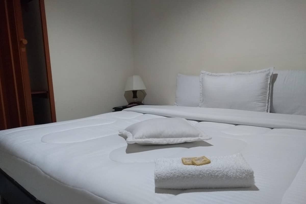 A neatly made bed with white bedding and pillows, a folded towel, and a lamp on a bedside table.