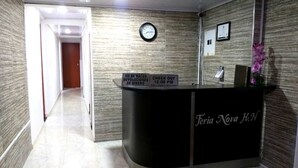 A reception desk with a clock above it, a sign indicating check-out times, and a nameplate reading "Feria Nova H.N".