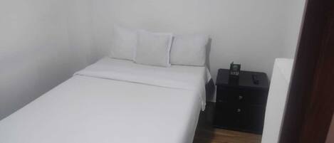 Una habitación pequeña y limpia con una cama individual, una mesita de noche y un estante en la pared.